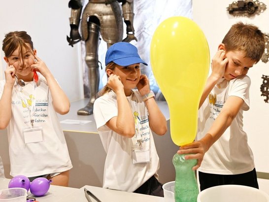 Kinder machen ein Experiment mit einem Luftballon und halten sich die Ohren zu