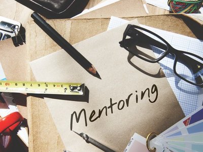 Stifte, Lineale usw. liegen auf einem Schreibtisch. Auf einem Blatt Papier steht "Mentoring" geschrieben