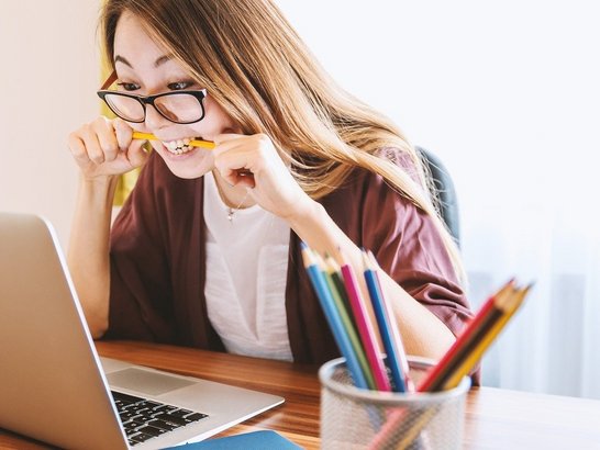 Eine Frau sitzt vor dem Laptop und beißt in einen Bleistift