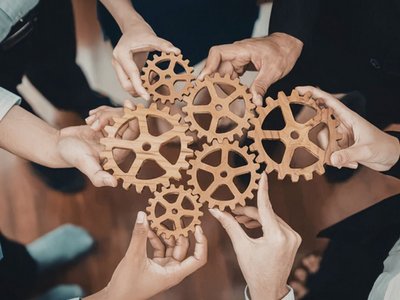 Personen halten Zahnräder zusammen als Symbol für Teamwork