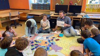 Kinder in Kreis rund um EU Teppich mit Wissenschaftsbotschafter Stephan Schweighofer