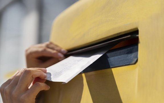 Brief wird in einen gelben Briefkasten geworfen