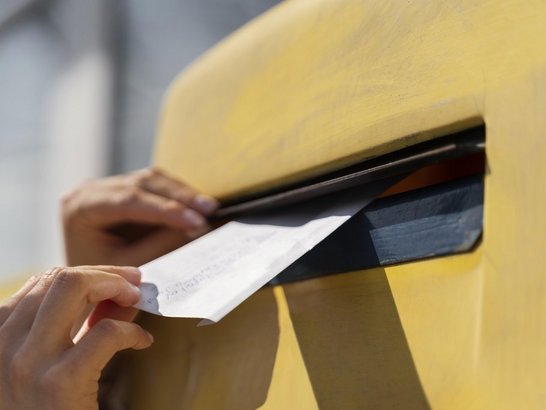 Brief wird in einen gelben Briefkasten geworfen