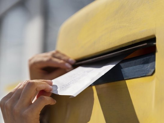 Brief wird in einen gelben Briefkasten geworfen