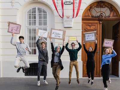 Junge Studierende hüpfen in die Luft und halten Schilder in der Hand